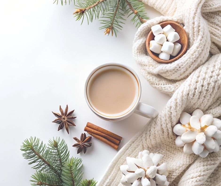 A cozy winter scene with a mug of hot chocolate topped with marshmallows, pine branches, cinnamon sticks, and a neutral blanket on a soft background
